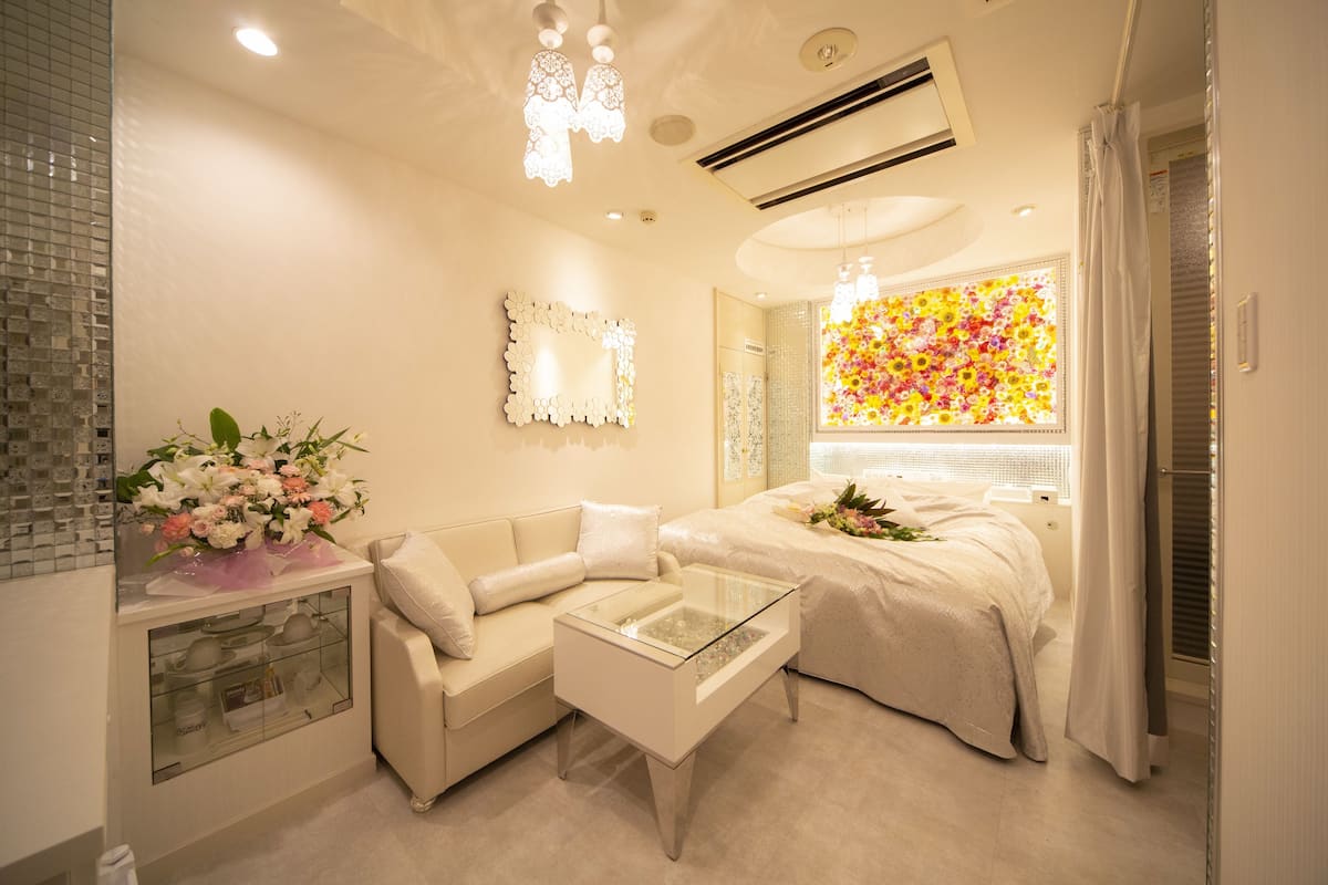 A modern bedroom with a glass coffee table, a sofa, a bed with a floral view, and a decorative mirror.