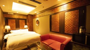 A hotel room with a bed, a red leather sofa, a glass coffee table, and a microwave. - Hotel Granhill - Adults Only (Tokyo)