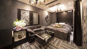 A modern bedroom with a glass coffee table, a sofa, a bed with patterned bedding, and a decorative mirror. - Hotel Granhill - Adults Only (Tokyo)