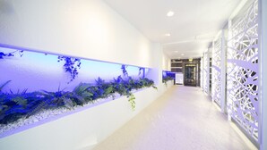 A hallway with a white wall, a decorative plant display, and a patterned floor. - Hotel Granhill - Adults Only (Tokyo)