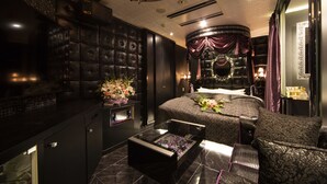 A luxurious bedroom with a large bed, a glass coffee table, and a dark, patterned sofa. - Hotel Granhill - Adults Only (Tokyo)