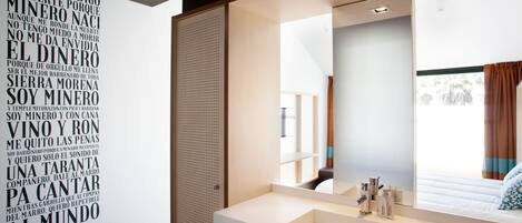 A modern bathroom with a large mirror, a white sink, and a wall with a word cloud design.