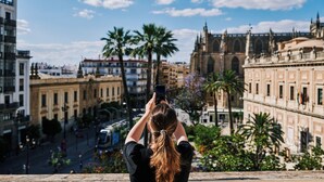 A person taking a photo of a cityscape with historic buildings and palm trees. - TOC Hostel Sevilla (Seville)