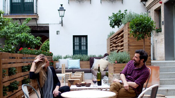 An outdoor patio with a round table, chairs, and a wooden planter with plants. - TOC Hostel Sevilla (Seville)