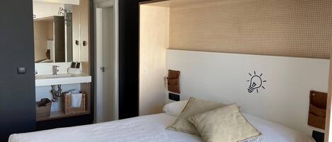 Un dormitori modern amb un llit gran, una tauleta de nit, una làmpada fixada a la paret i un mirall sobre el benedic.