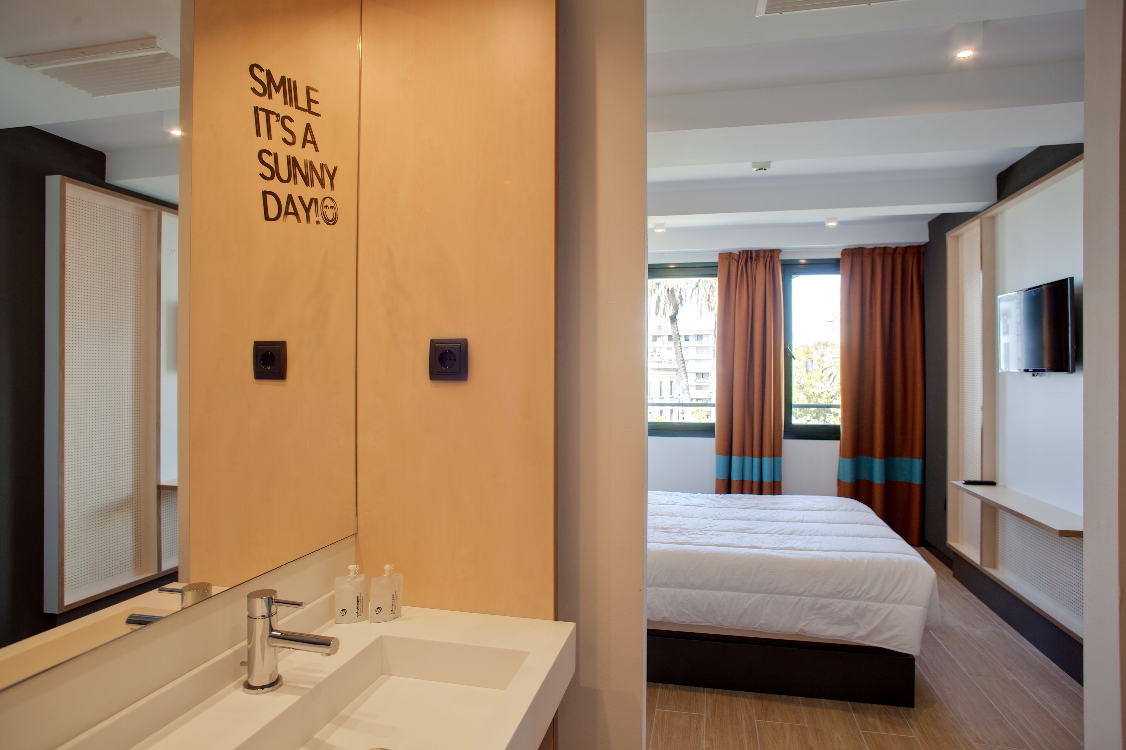 A hotel room with a large mirror, a sink, a bed, and a television.