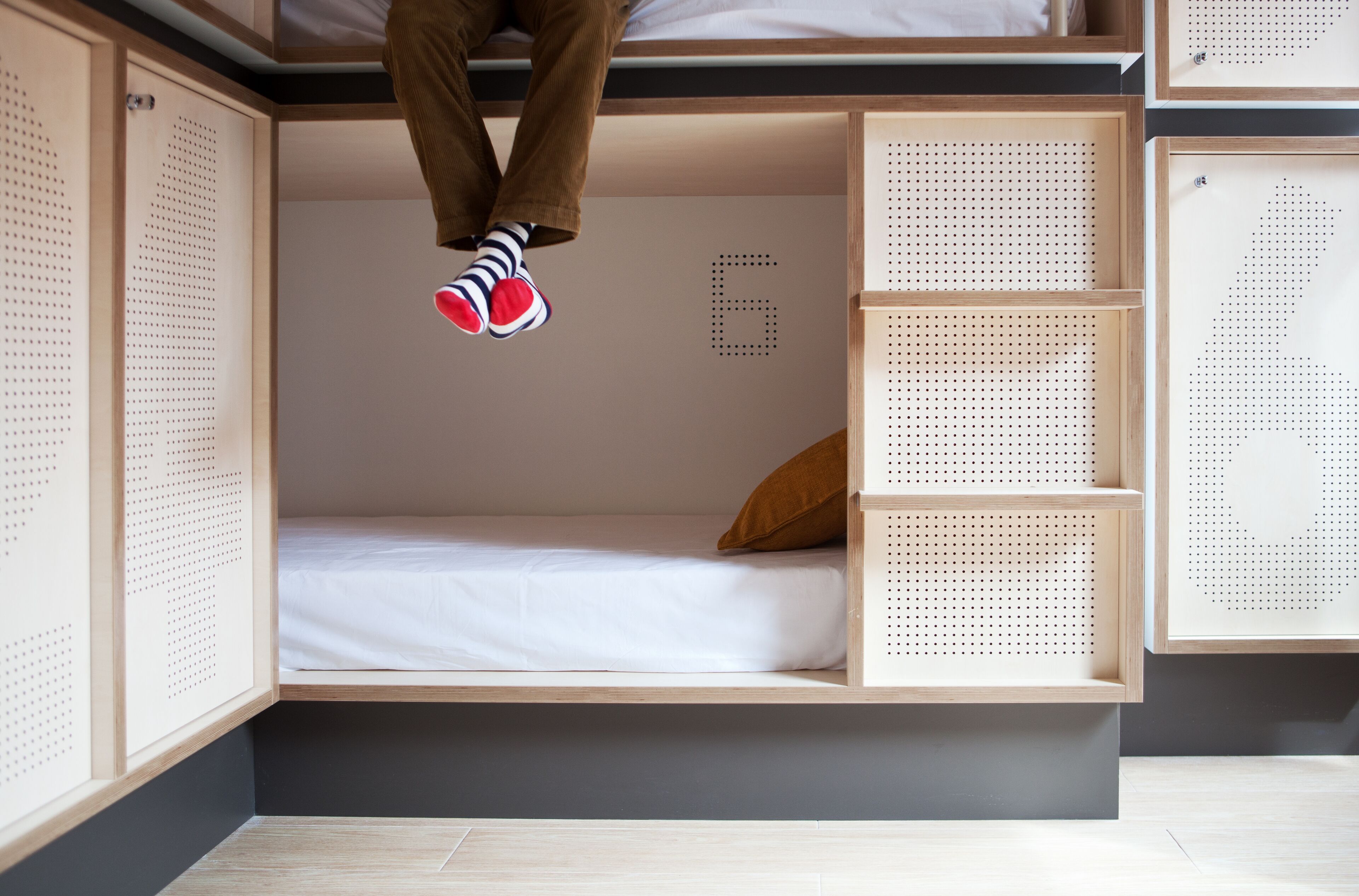 A bunk bed with a wooden frame, a white mattress, and a single brown pillow.