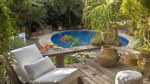 A wooden deck with a lounge chair, a small table, and a decorative stone planter. - Pousada Pilar (Arraial do Cabo)