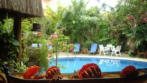 A swimming pool surrounded by lush greenery and outdoor seating. - Pousada Pilar (Arraial do Cabo)