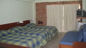 A hotel room with two beds, a television, and a brick wall. - Pousada Pilar (Arraial do Cabo)
