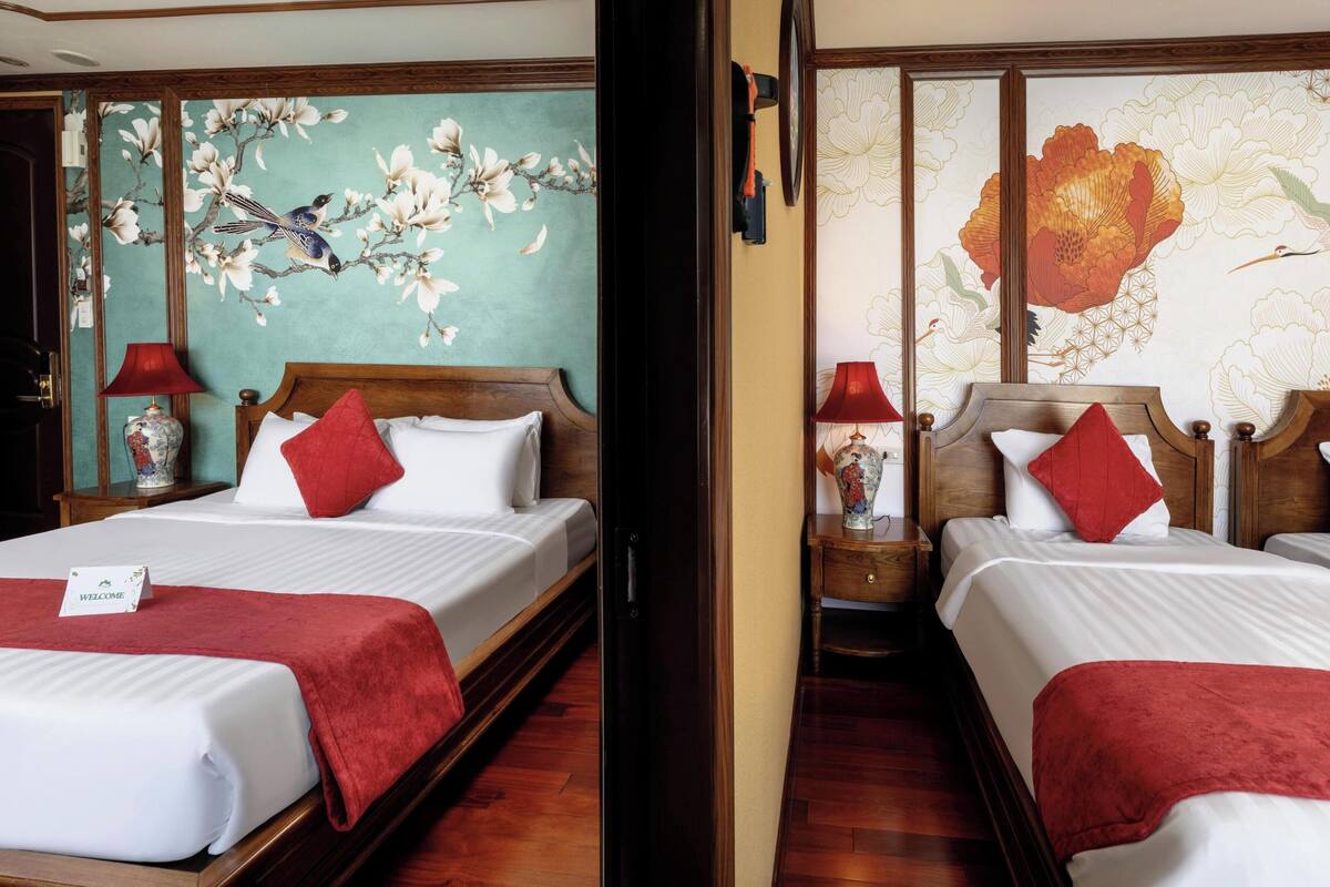 Habitación de hotel con dos camas, cabeceros de madera, decoración floral en la pared y un cartel de bienvenida rojo.