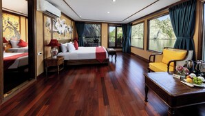 Habitación de hotel con cama, sofá, mesa de comedor con fruta y vista a un cuerpo de agua.