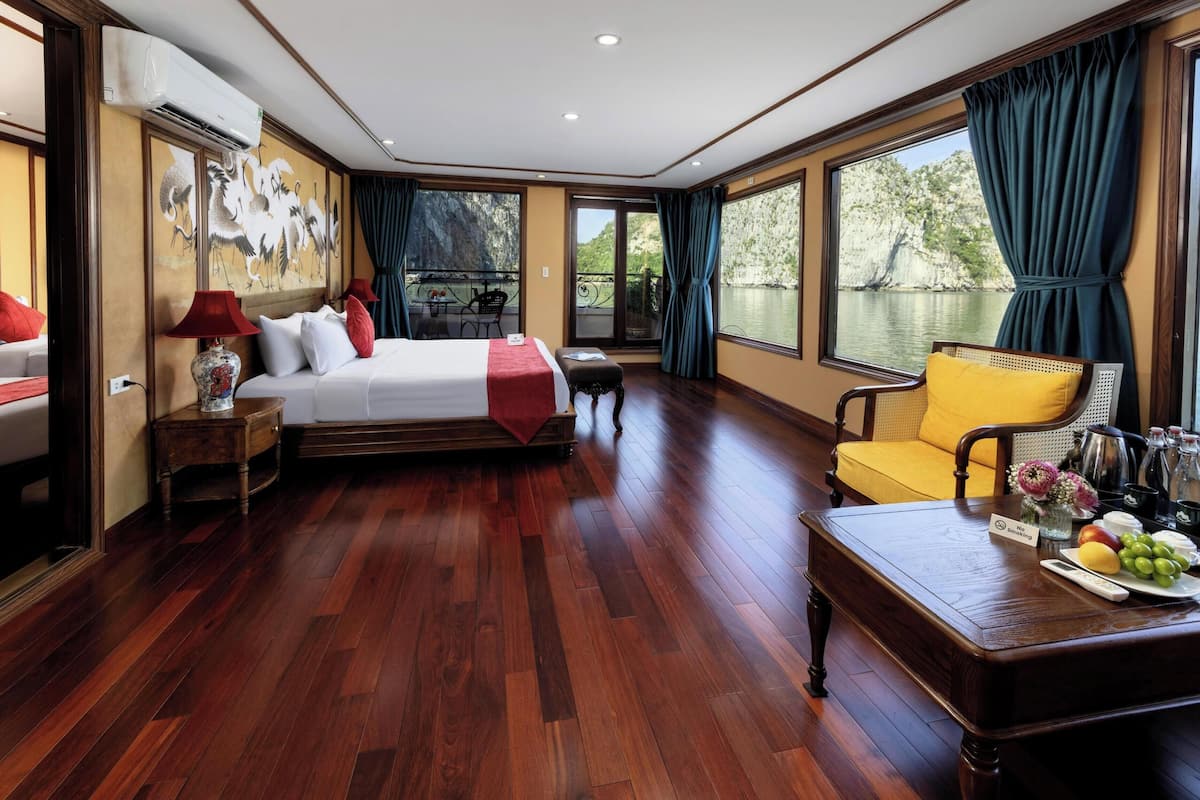 Habitación de hotel con cama, sofá, mesa de comedor con fruta y vista a un cuerpo de agua.