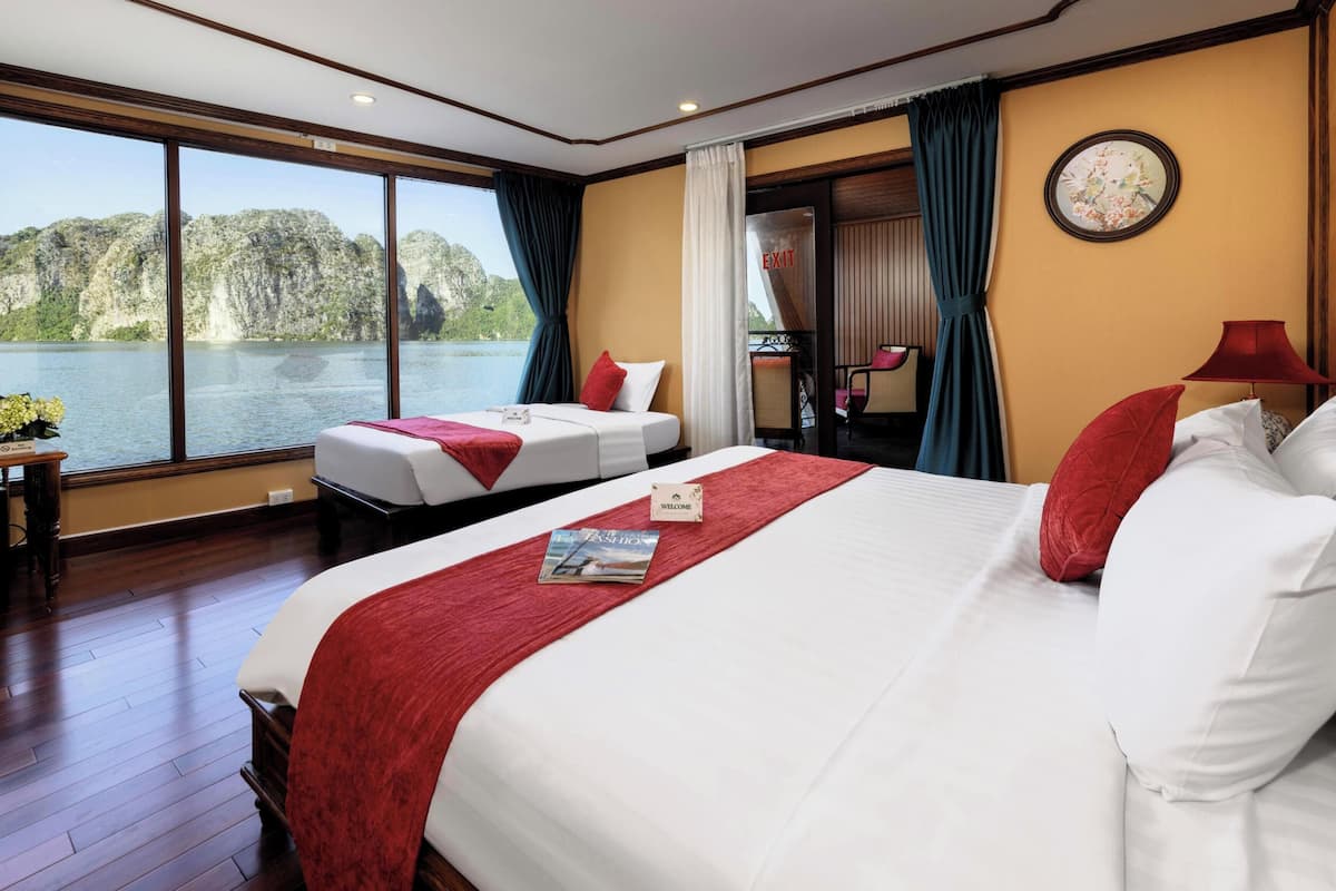 Habitación de hotel con una cama grande, una cama más pequeña, vista a un lago y un balcón con una silla.