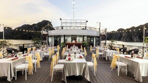 Terraza de restaurante con mesas dispuestas para comer, con vista a un cuerpo de agua y colinas.