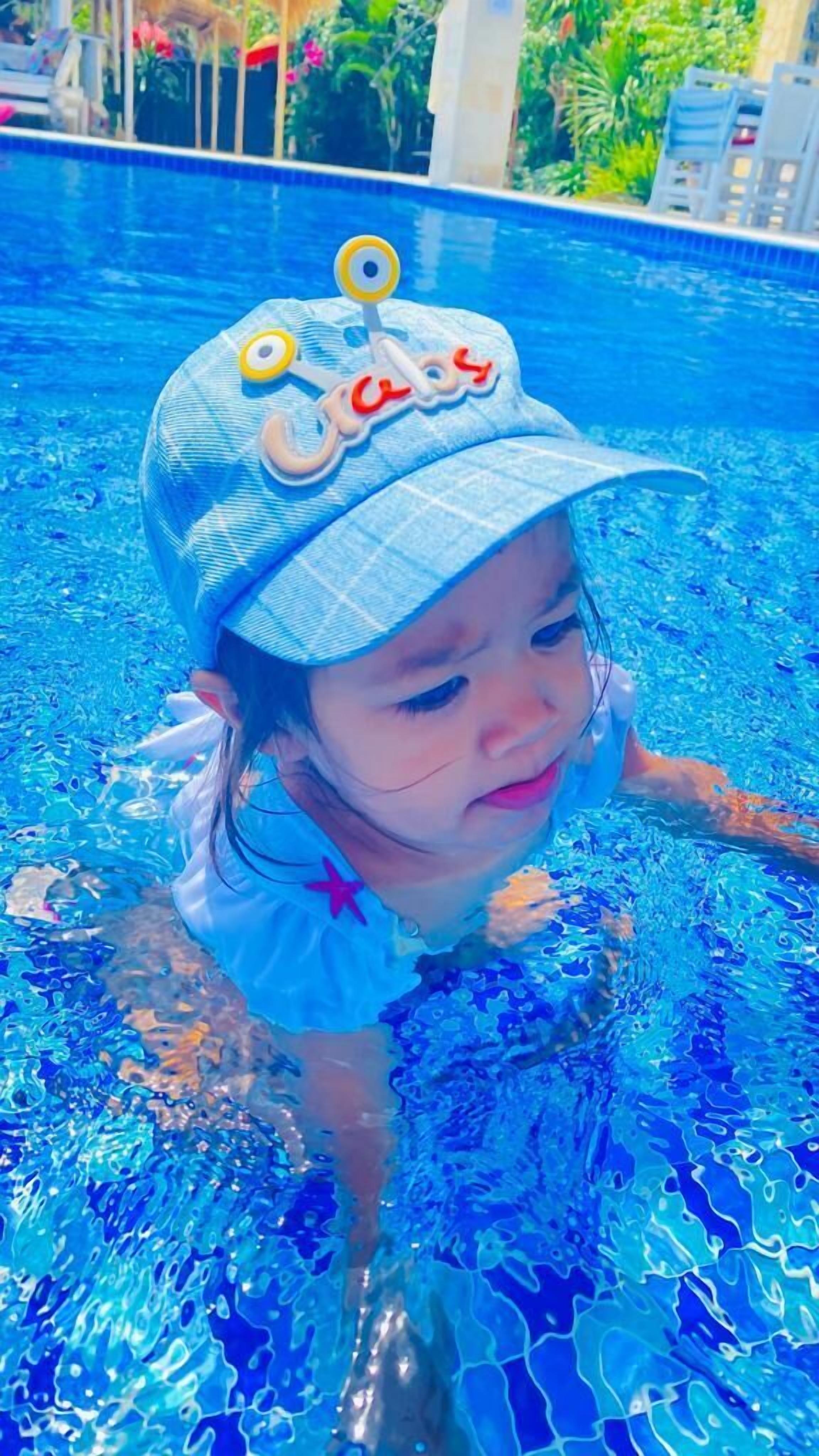A child in a swimming pool wearing a hat with a cartoon character and the word "babies".