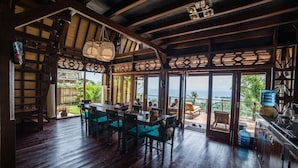 A spacious dining area with a wooden ceiling and large windows overlooking a lush garden. - Villa Umbrella (Senggigi)