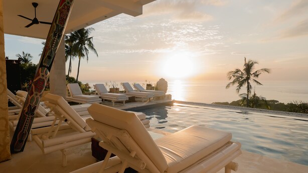 A poolside area with lounge chairs and a view of the sunset over the ocean. - Villa Umbrella (Senggigi)