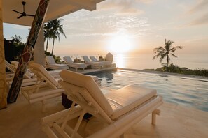 A poolside area with lounge chairs and a view of the sunset over the ocean. - Villa Umbrella (Senggigi)