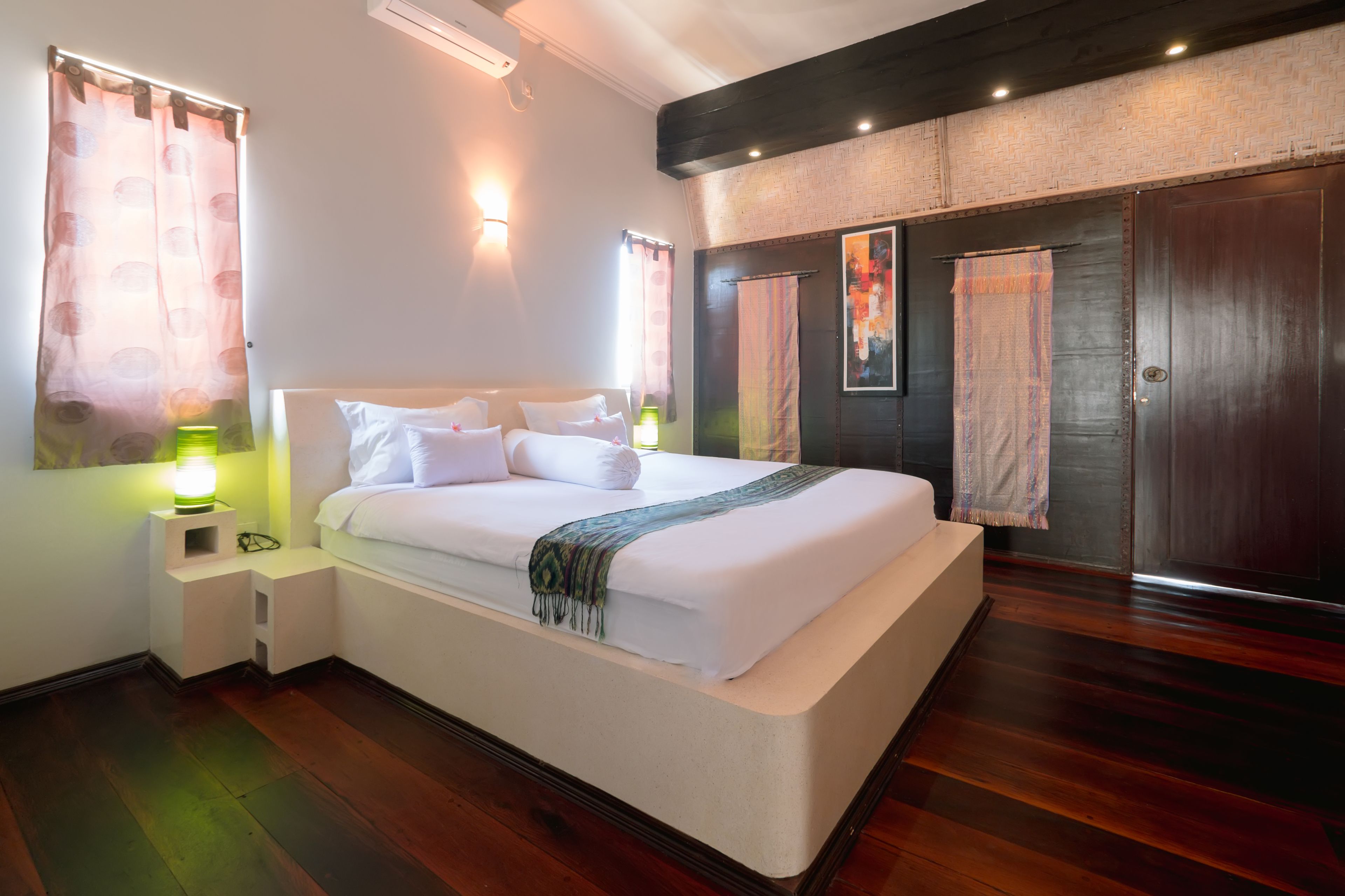 Een moderne hotelkamer met een groot bed, bedlampjes, een houten vloer en een donkerhouten garderobe.