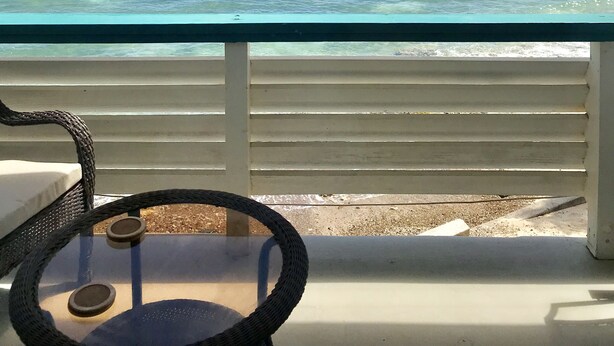 Un balcon offrant une vue dégagée sur l’océan, un bateau et les reliefs lointains.