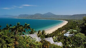 A coastal landscape with a beach, clear blue waters, and a mountainous backdrop. - Beach Club Port Douglas 3 Bedroom Luxury Apartment (Port Douglas)