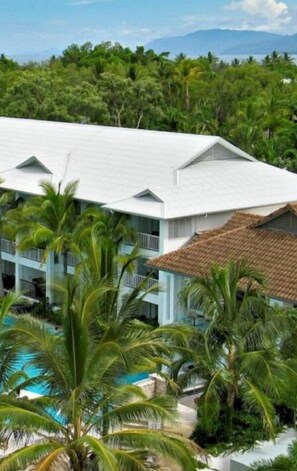 A resort building with a white exterior, a pool, and palm trees. - Beach Club Port Douglas 3 Bedroom Luxury Apartment (Port Douglas)