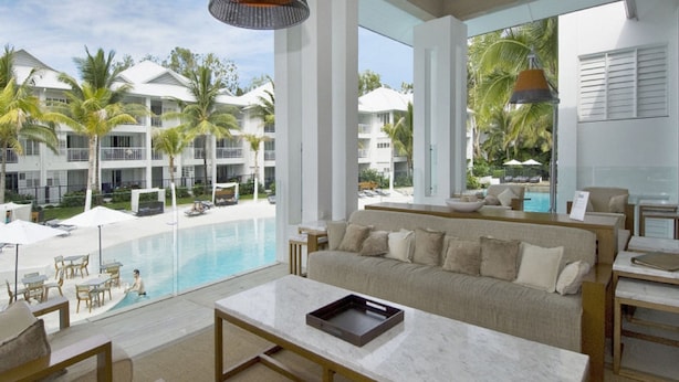 A modern hotel room with a large window overlooking a pool and palm trees. - Beach Club Port Douglas 3 Bedroom Luxury Apartment (Port Douglas)