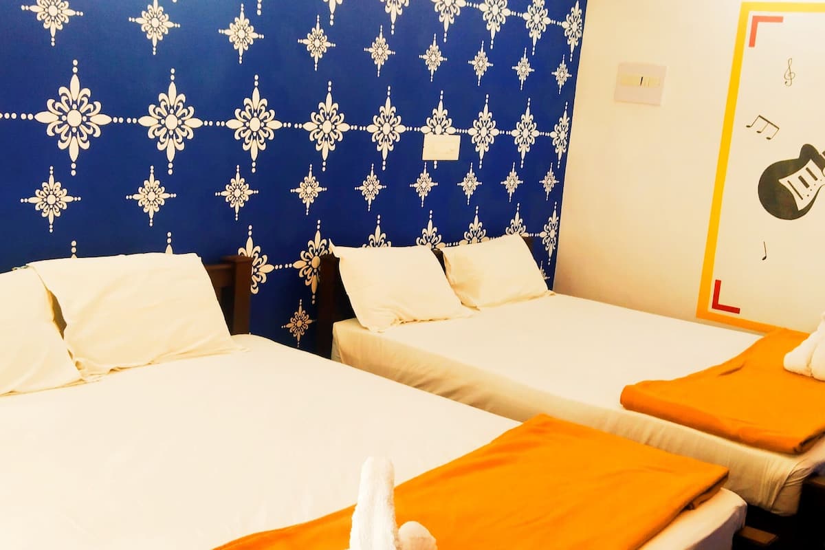 Two single beds with white linens and orange towels, a blue patterned wall, and a guitar illustration on the wall.
