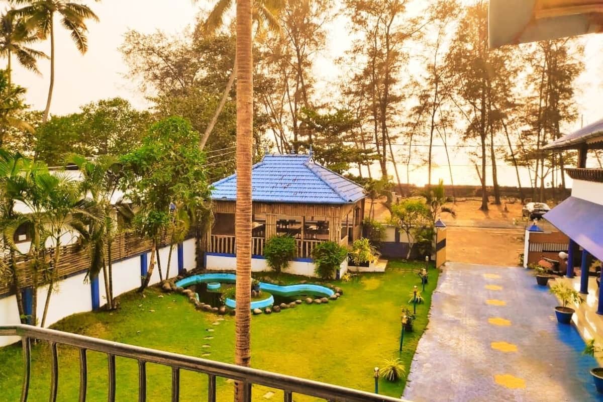 A courtyard with a blue-roofed building, surrounded by palm trees and a small water feature.