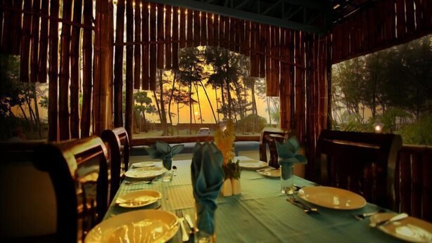 An outdoor dining area with bamboo walls, a view of trees, and a table set for two. - Mare blu Resort (Kochi)