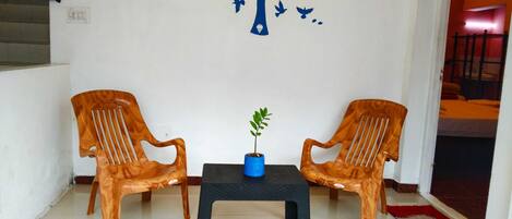 Una habitación con dos sillas de madera, una mesa pequeña y un mural en la pared con un árbol y pájaros.