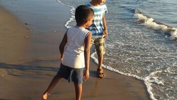 Two children walking along a sandy beach with waves coming in.