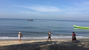 A beach with three people walking along the shore, a boat in the water, and a green kayak on the sand. - Mare blu Resort (Kochi)