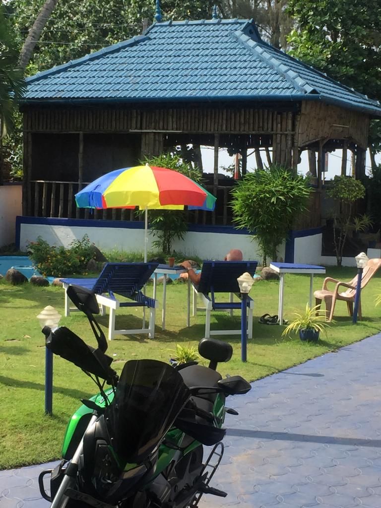 Un porxo amb teulada blava, envoltat d'una piscina, cadires i una moto.