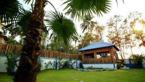 A small, single-story building with a blue roof, surrounded by lush greenery and palm trees. - Mare blu Resort (Kochi)