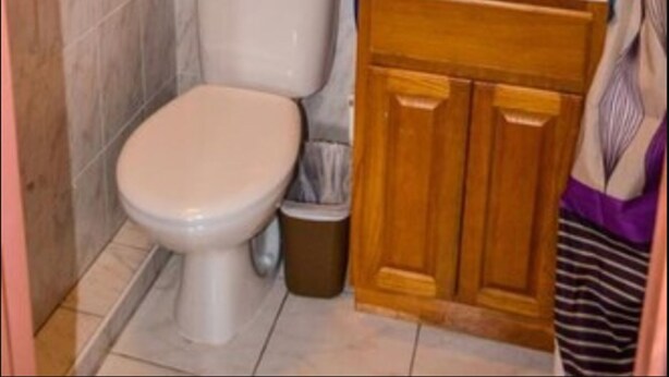A bathroom with a toilet, sink, and wooden cabinet. - Fantastic Hotel (Marigot)
