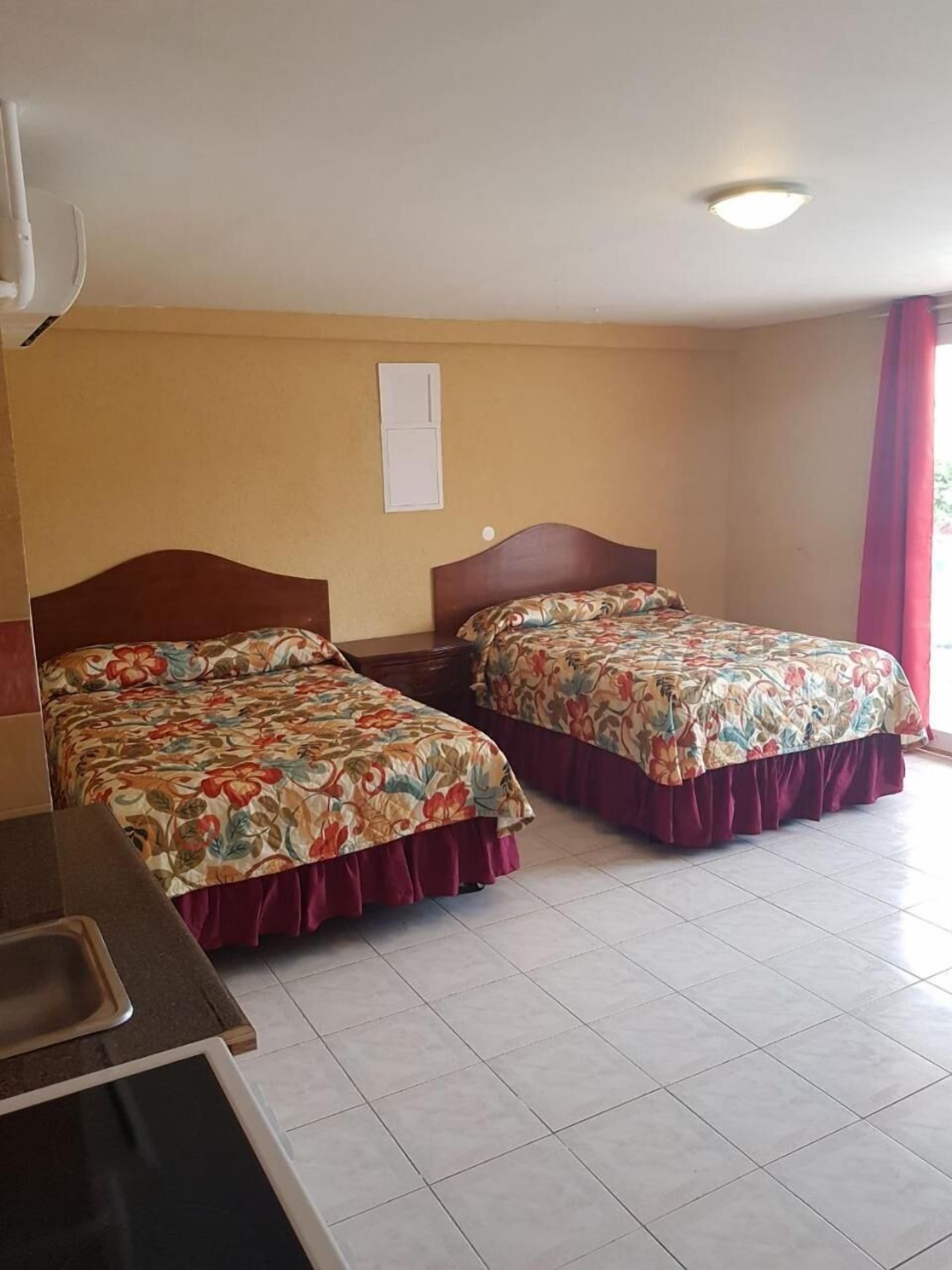 Habitación de hotel con dos camas, un escritorio y una ventana con cortinas.