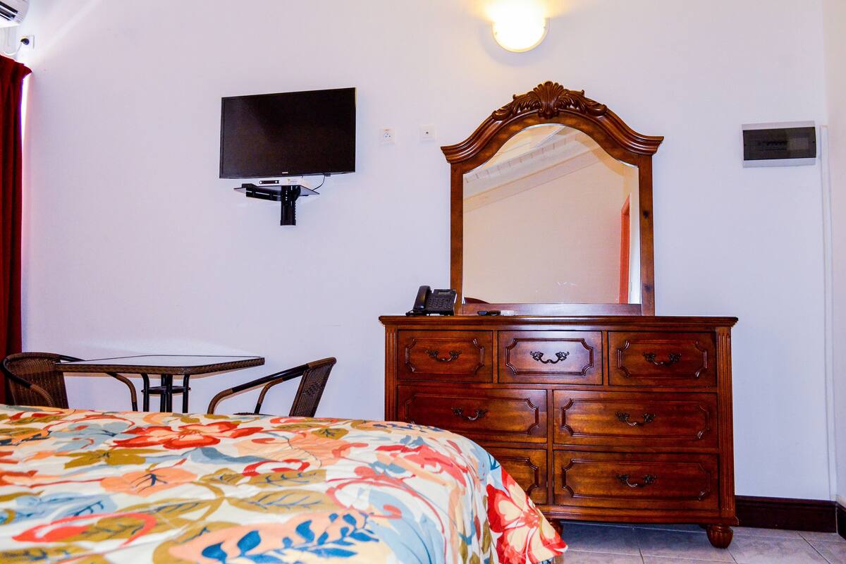 A bedroom with a bed, a dresser, a television, and a small table.