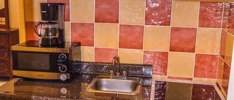 A compact kitchen with wooden cabinets, a microwave, a coffee maker, a sink, and a built-in oven.