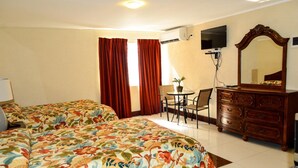 A hotel room with two beds, a desk with a chair, a dresser, a TV, and a large mirror. - Fantastic Hotel (Marigot)