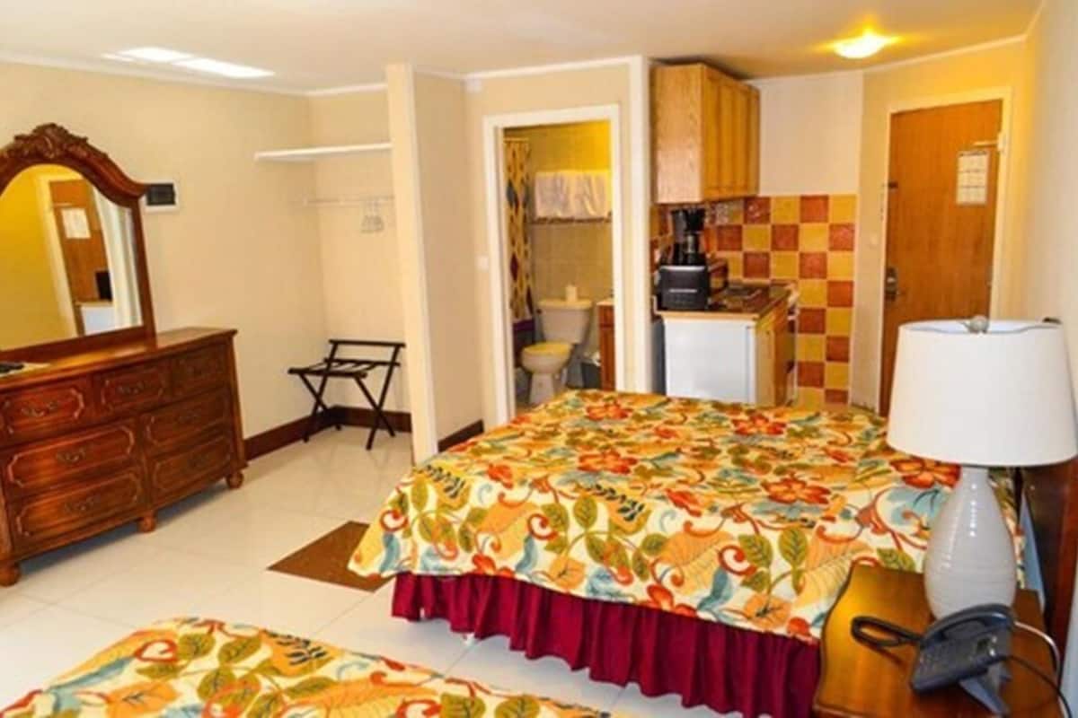 A hotel room with a bed, a dresser, a desk with a lamp, and a bathroom visible through an open door.