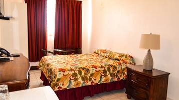 Una habitación de hotel con cama, escritorio, silla, cómoda y lámpara.