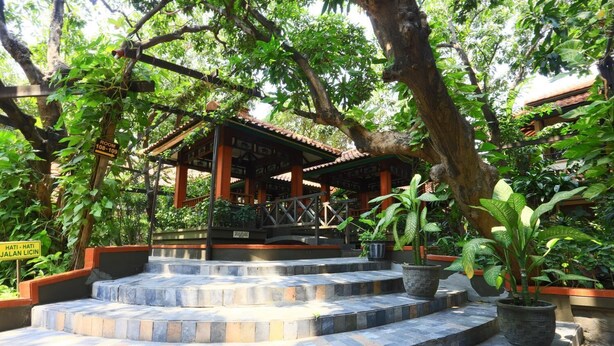 A traditional wooden pavilion with stone steps leading up to it, surrounded by lush greenery.