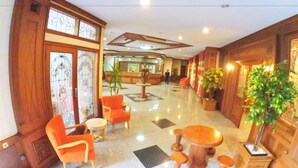 A lobby with wooden paneling, a reception desk, several orange chairs, a round table, and potted plants.