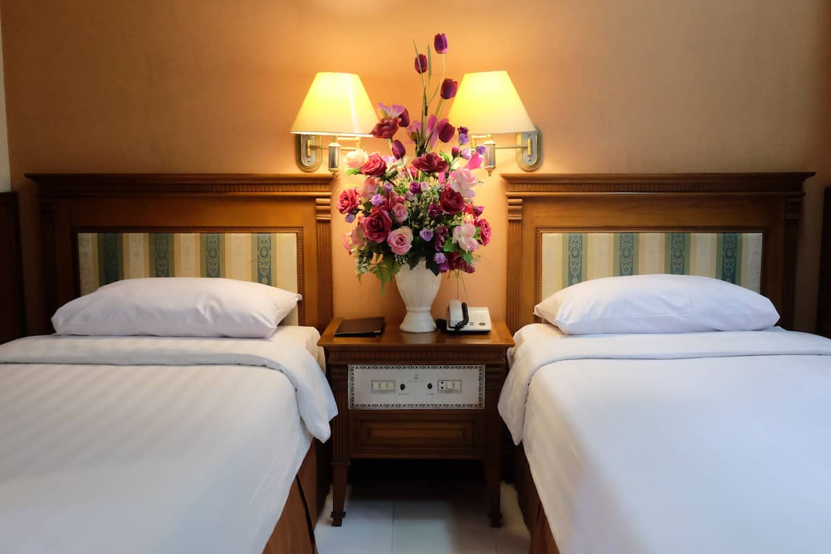 Een hotelkamer met twee bedden, een nachtkastje met een lamp, een bloemenvaas en een telefoon.