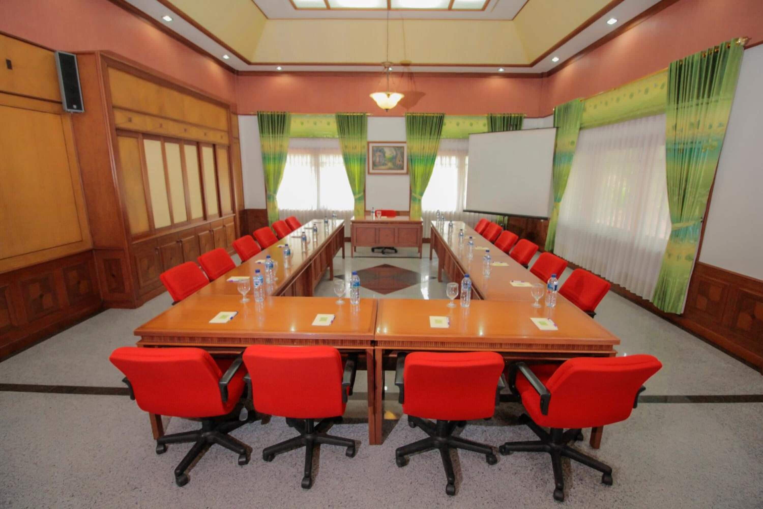 A conference room with a long table, red chairs, and a whiteboard.