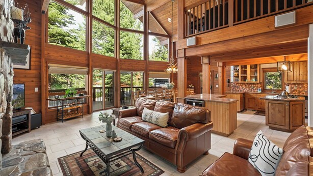 A spacious living area with a large wooden ceiling, a leather sofa, a coffee table, and a stone fireplace. - Donner Lake Retreat | Queen Suite, Games, Near Lake, Golf & Trails (Truckee)