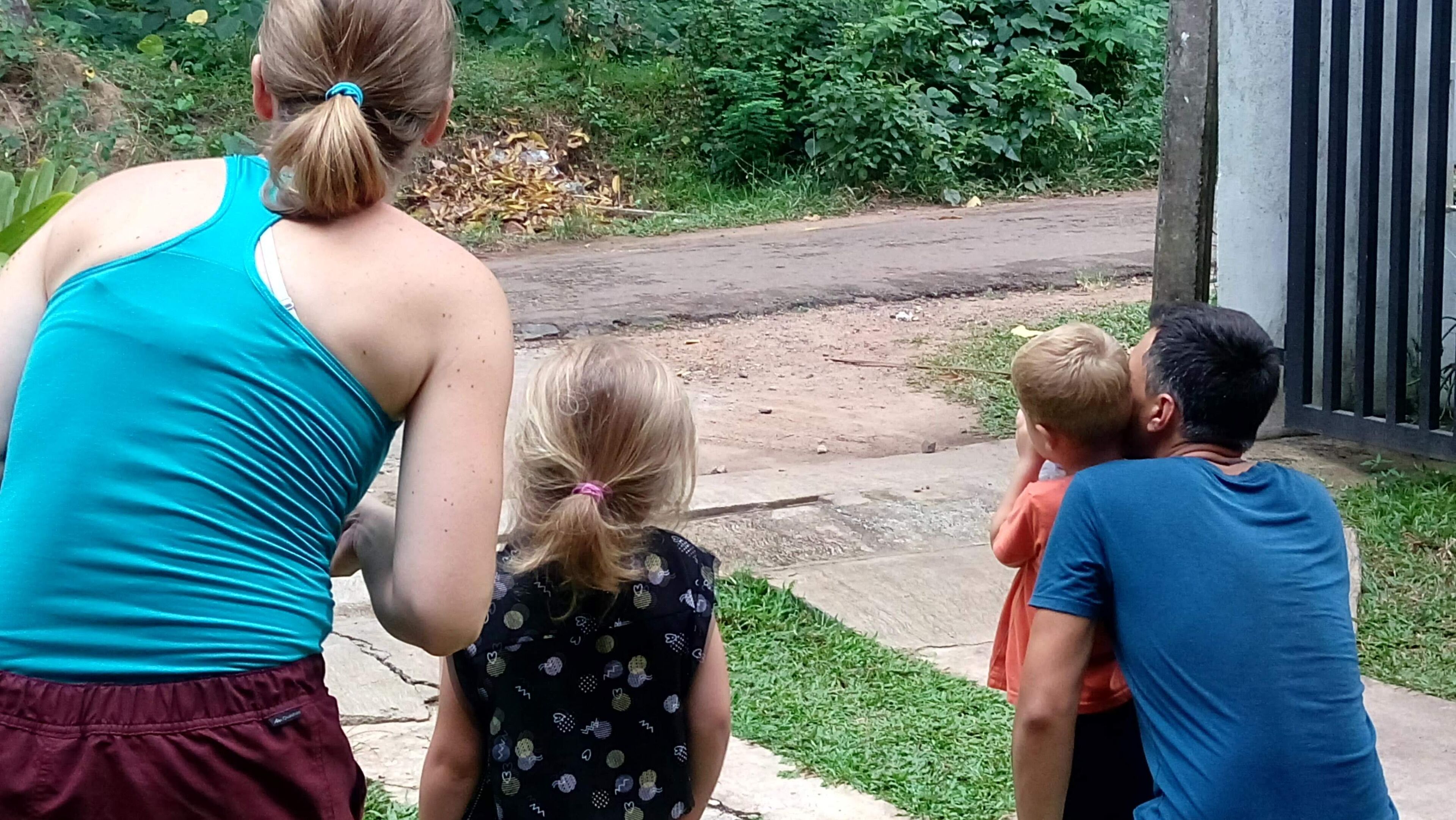 A family of four standing on a concrete path with a garden and a building in the background.