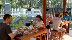 Un grupo de personas cenando al aire libre en una mesa de madera, con varios platos y bebidas.